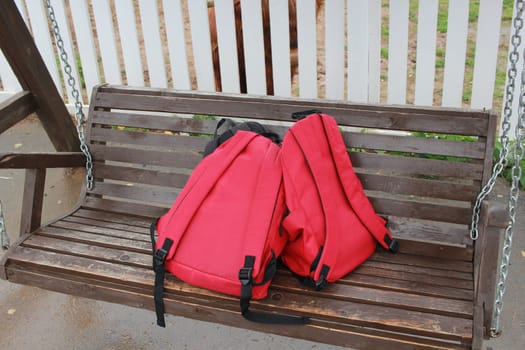 Photo two red children's backpacks are lying on a wooden hanging swing. Rest. School. Holidays.