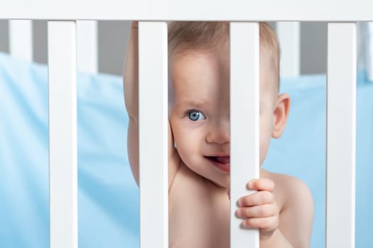 A baby in a playful mood looks slyly through the crib fence.