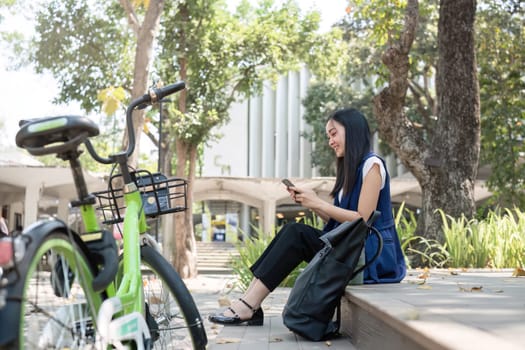 Asian business woman sitting and working in a nature park Travel by bicycle to save the environment.