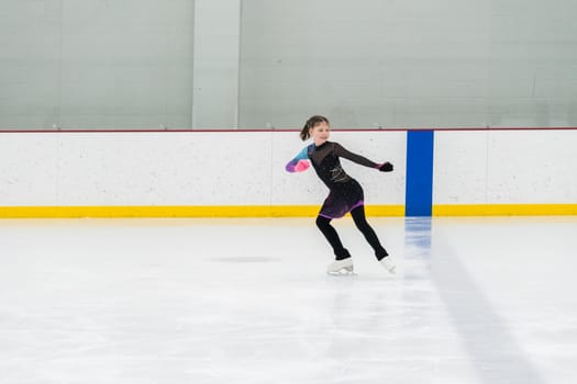 Young girl perfecting her figure skating routine while wearing her competition dress at an indoor ice rink.