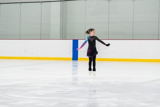 Young girl perfecting her figure skating routine while wearing her competition dress at an indoor ice rink.