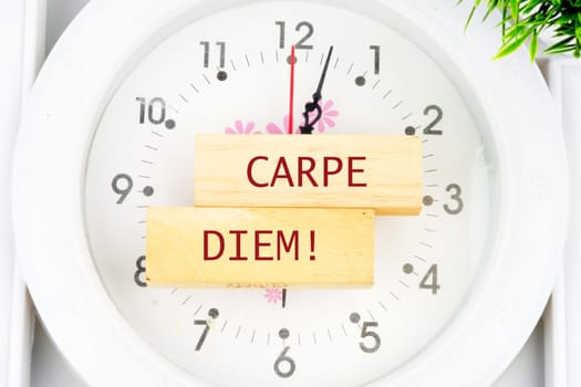 The Latin phrase Carpe Diem, a quote from Horace, means seize the moment. Live in the present written on the wooden blocks on the clock with hands