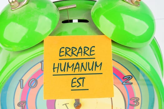 Latin quote Errare humanum est, meaning It is human nature to make mistakes. Mistakes are inherent in human existence. Text written on the orange sticker on the alarm clock