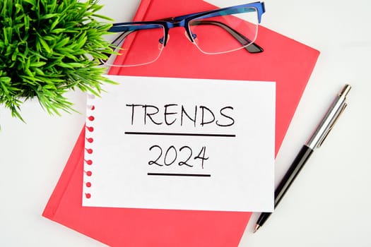 The evaluation methods, popular topics, and new trends in business. TRENDS 2024 written on a piece of paper on a red notebook on a white background