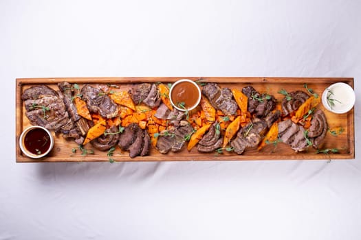 An appetizing assortment of meats, potatoes, and sauces beautifully presented on a wooden board for a hearty and satisfying meal.