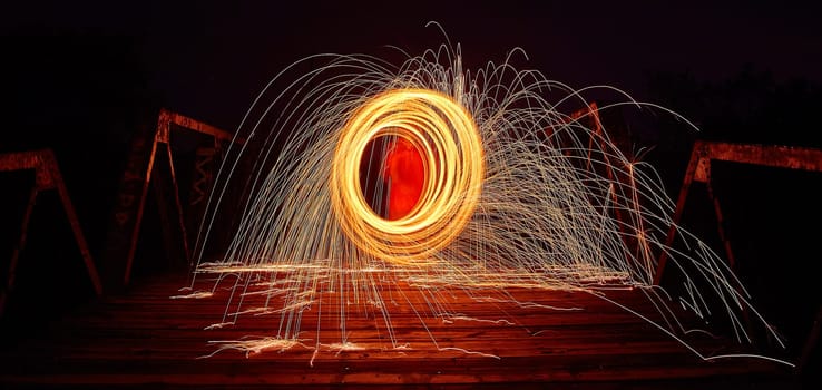 Fiery long exposure capture of steel wool spinning on an old bridge in Fort Wayne, Indiana, 2017, showcasing a vibrant spectacle of light and motion.