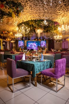 An elegant restaurant interior with purple chairs, green tablecloths, chandeliers, and decorative wall flowers creating a cozy atmosphere.