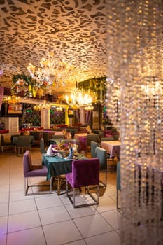 An elegant restaurant interior with purple chairs, green tablecloths, chandeliers, and decorative wall flowers creating a cozy atmosphere.