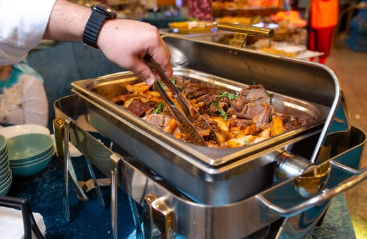 A buffet food warmer filled with delicious beef. The beef is cooked to perfection and is served with a variety of sauces and sides.