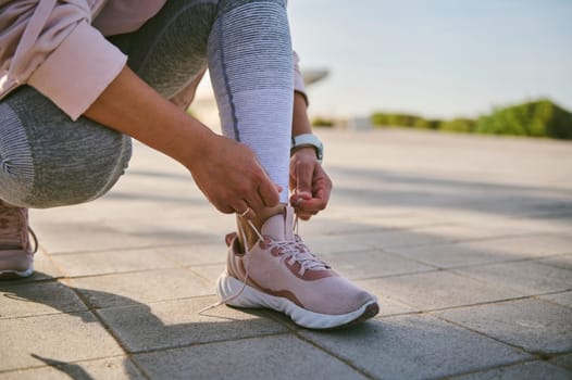 Cropped view of sportswoman tying shoe laces, getting ready for morning run on the urban environment. Young active woman running jogging exercising in the park. Fitness, healthcare and dieting concept
