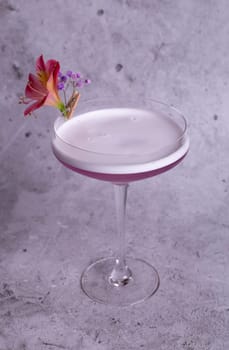 Elegant image of a pink cocktail in a glass with a flower garnish on a gray background, exuding class and sophistication.