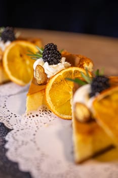 A decadent display of four slices of creamy cheesecake adorned with vibrant orange slices and juicy blackberries on a dainty white doily.