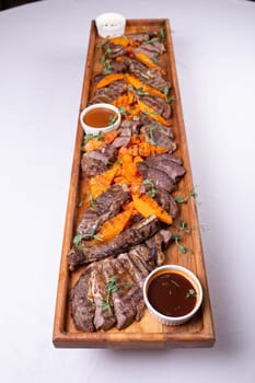 An appetizing assortment of meats, potatoes, and sauces beautifully presented on a wooden board for a hearty and satisfying meal.