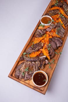 An appetizing assortment of meats, potatoes, and sauces beautifully presented on a wooden board for a hearty and satisfying meal.