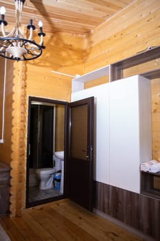 Wooden house bathroom with corner shower, toilet, sink. Glass door, wood walls floor. Cozy, modern, rustic design.