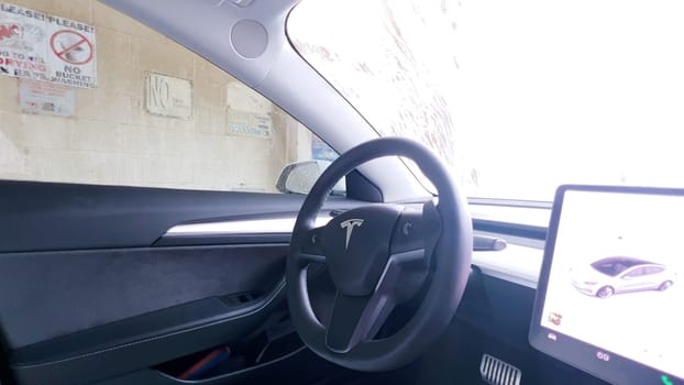 Denver, Colorado, USA-February 17, 2024-The interior of a Tesla Model 3 is shown from the driver’s perspective during a car wash, highlighting the vehicle’s modern design and dashboard display while water streams down the windshield.