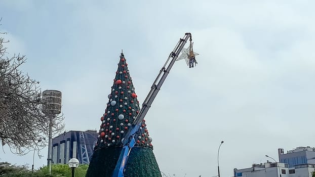 Man on crane decorating big Christmas tree in the city