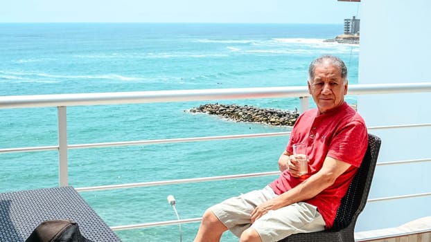 Mature man sitting on a balcony overlooking the sea with a cocktail