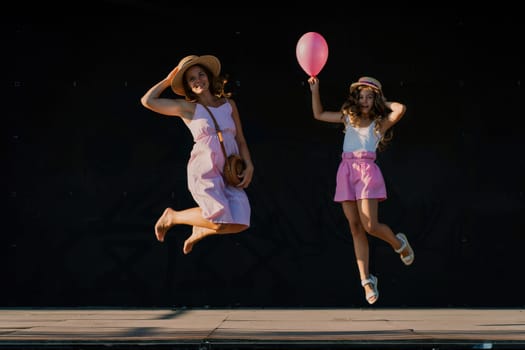 mother and daughter jumping in pink dresses with loose long hair on a black background. Enjoy communicating with each other.