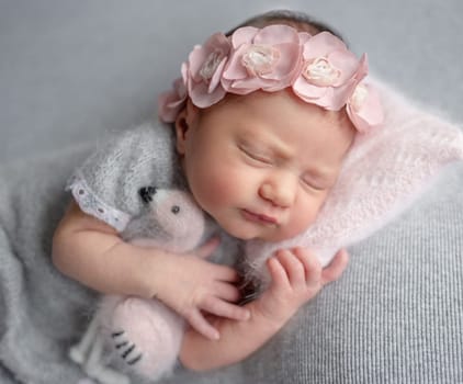 Newborn Girl Sleeps In Gray Dress With Flamingo Toy During Baby Photoshoot In Studio