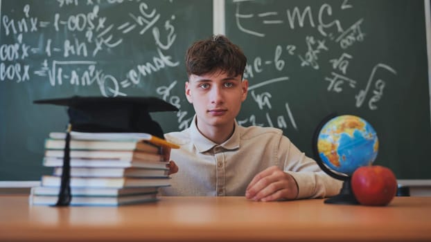 Portrait of a high school student against a background of blackboard, globe and books with cap