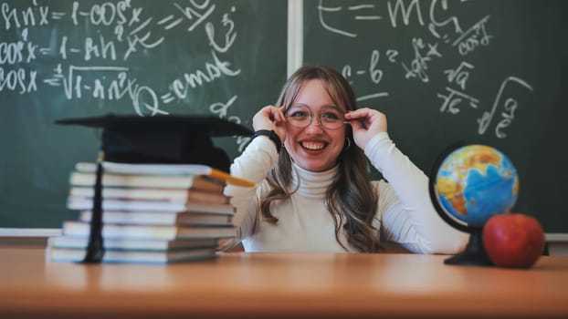 A schoolgirl wearing glasses poses against a background of books, an apple, a globe and a graduation cap