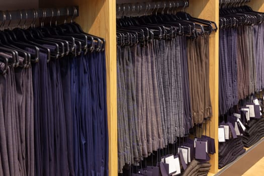 Men's classic trousers on hangers in a boutique. Showcase with many men's trousers hanging on hangers in stock on hangers in a men's clothing store.