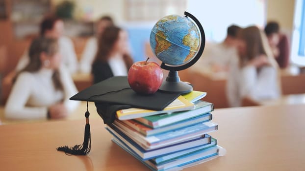 A globe of the world with textbooks and a college graduate's cap in a school classroom during class