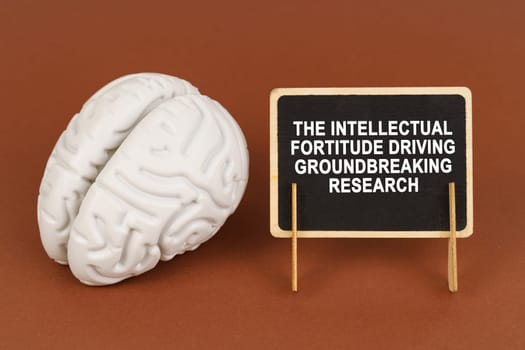 On a brown background, a model of the brain and a sign with the inscription - The intellectual fortitude driving groundbreaking research. Business and technology concept.