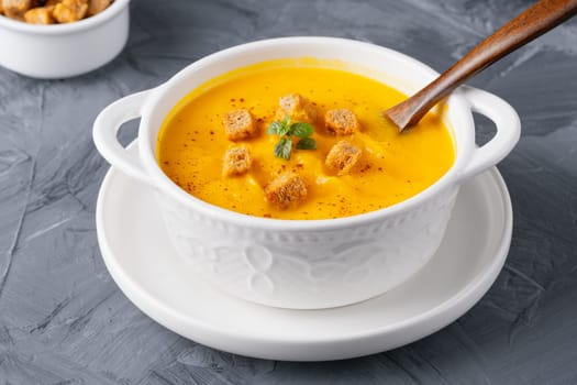 Pumpkin soup with croutons on grey background.
