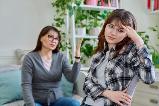 Conflict between mother and teen daughter, offended teenage girl sitting with back to upset arguing mother, on couch at home. Family, difficulties, problems, differences between two generations