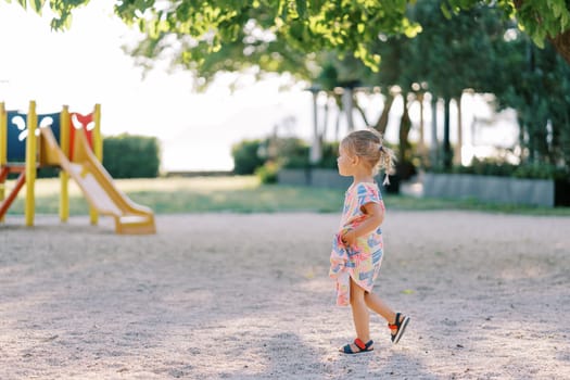 Little girl walks on the playground looking at the slide. Side view. High quality photo