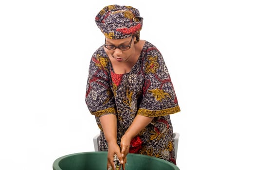 African woman standing above the laundry bowl washing clothes isolated on white background.