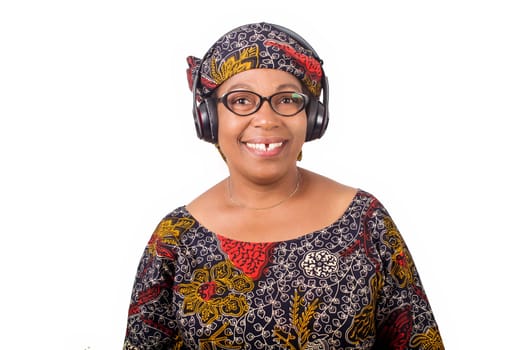 smiling mature african woman in african loincloth and scarf listening music with headphones on white background
