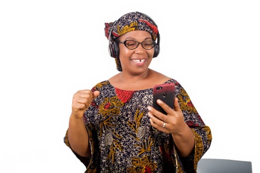 mature african woman in loincloth listening music using headphones and cellphone having hand gesture