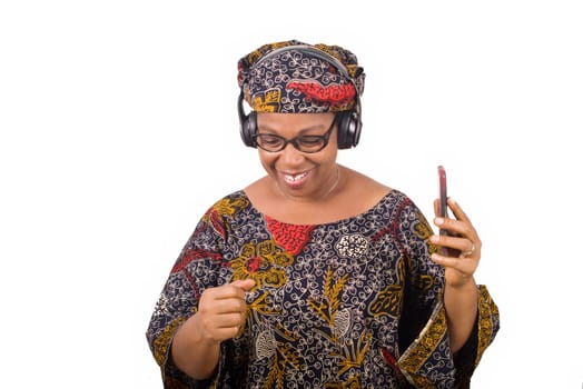 mature african woman in loincloth listening music using headphones and cellphone having hand gesture