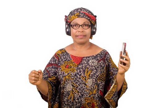 mature african woman in loincloth listening music using headphones and cellphone having hand gesture