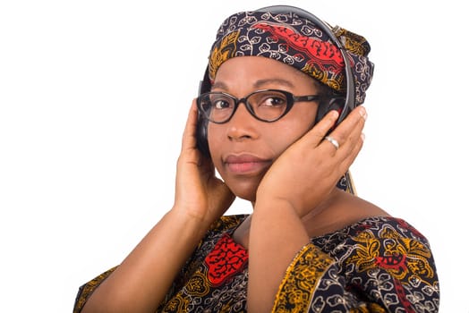 beautiful african american woman listens to music. African woman in traditional dress with a head scarf standing in profile and holding a headset in the ear while looking at the camera