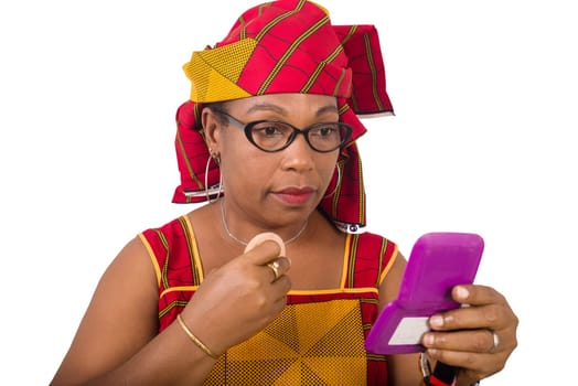beauty, makeup and elderly concept in red african outfit - senior woman applying powder to face looking in small mirror on white background