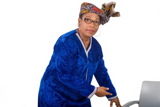 mature woman in blue dress on white background showing chair while looking at camera