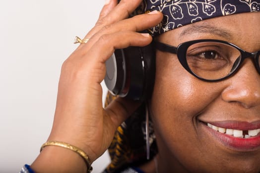 mature woman standing on white background listening to music using headphones while smiling.