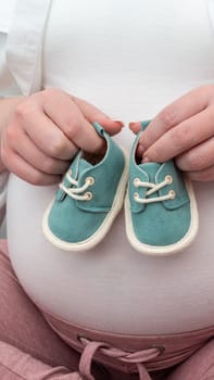 Expecting mother holding baby shoes on belly. Maternity prenatal care and pregnancy concept