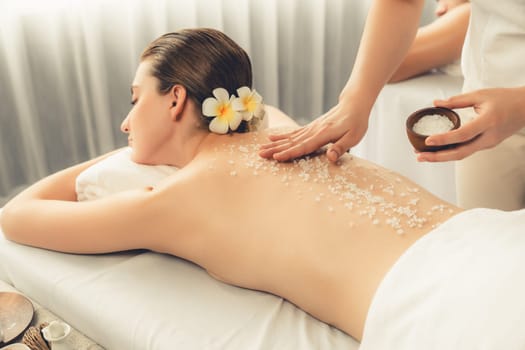 Blissful couple customer having exfoliation treatment in luxury spa salon with warmth candle light ambient. Salt scrub beauty treatment in health spa body scrub. Quiescent