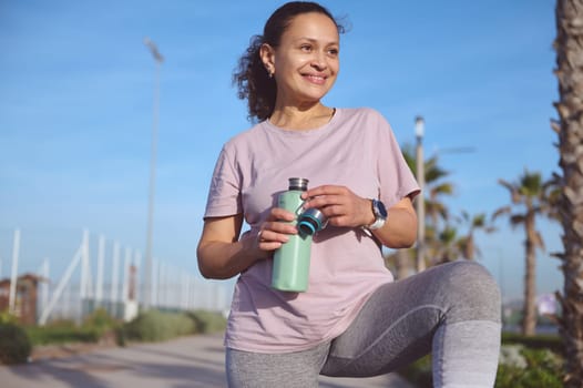 Smiling happy female athlete, determined sportswoman drinking water after playing sports on the beach.