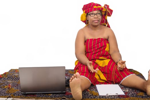 mature woman in loincloth sitting on the floor looking at the camera smiling with a notepad in front of her.