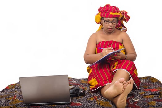 mature woman in loincloth sitting on the floor writing on her note pad.