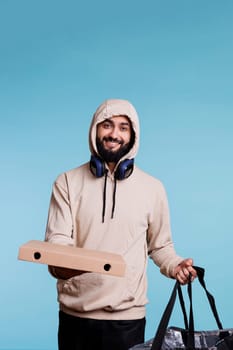 Smiling food delivery service arab courier holding pizza box and backpack portrait. Cheerful young man in hood giving fastfood takeaway order and looking at camera with carefree expression