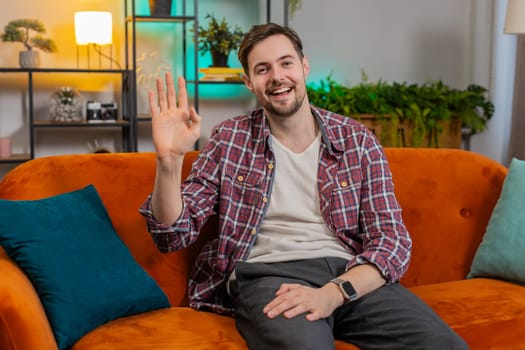 Portrait of cheerful young man in plaid shirt smiling at camera and waving gesturing hello, hi, greeting or goodbye. Happy Caucasian guy making video webcam conference call with friend at home room