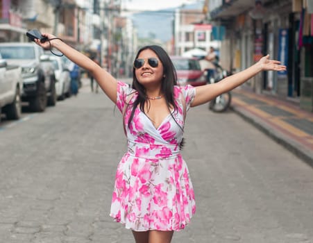 A happy young tourist celebrates life with open arms in the middle of a bustling urban road, exuding freedom and joy on her vacation trip. High quality photo