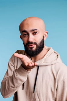 Young romantic arab man expressing affection while sending air kiss portrait. Charming handsome person wearing casual hoodie clothes showing love and flirting while looking at camera